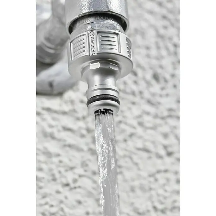Gardena Hahnstück - Gewindegröße Wasserhahn: 26,5 mm (G 3/4“) - Nahaufnahme eines Wasserhahns der Marke Gardena, aus dem Wasser fließt, vor einer unscharfen, weißen Wand.