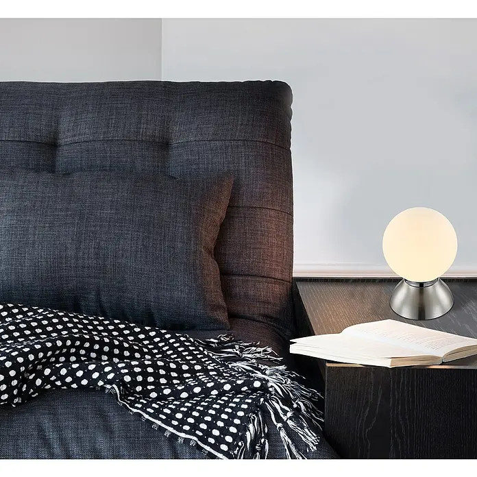 Globo Lámpara de sobremesa LED - 4 W, Blanco, Opal, Blanco cálido - Primer plano de una moderna lámpara de mesa redonda con base metálica sobre una mesita de noche junto a una cama.