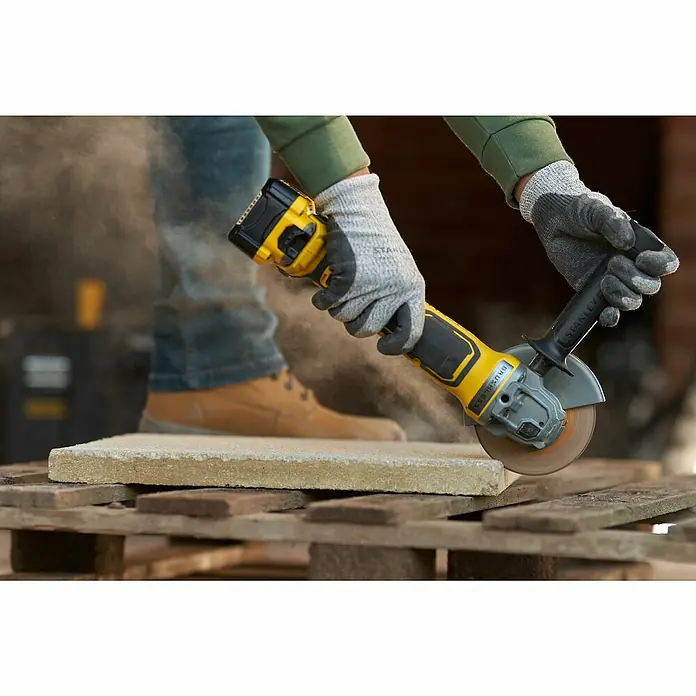 Stanley FatMax Akku-Winkelschleifer SFMCG700B-XJ - Ohne Akku, Durchmesser Scheibe: 125 mm - Eine Person benutzt eine gelbe Stanley-Flex mit Akku zum Schneiden eines Pflastersteins.