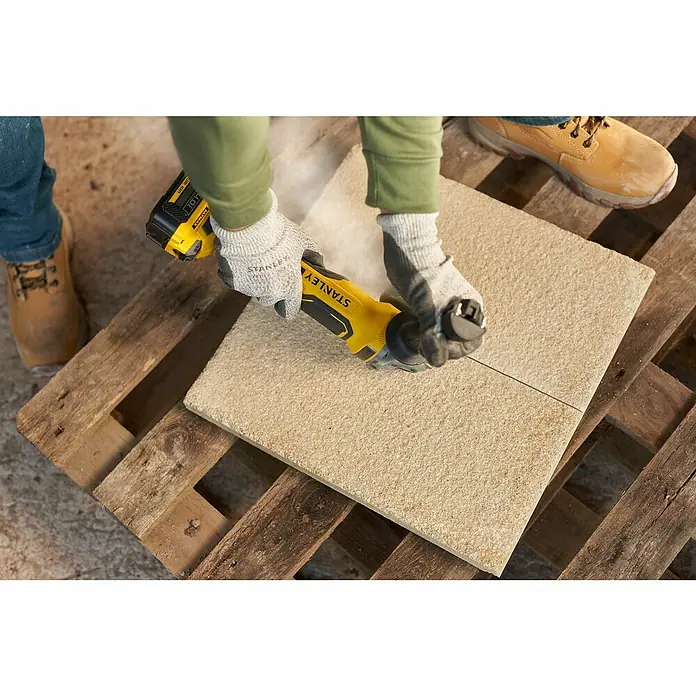 Stanley FatMax Akku-Winkelschleifer SFMCG700B-XJ - Ohne Akku, Durchmesser Scheibe: 125 mm - Nahaufnahme eines gelben Stanley-Multifunktionswerkzeugs, das einen Stein auf einer Holzpalette schneidet.