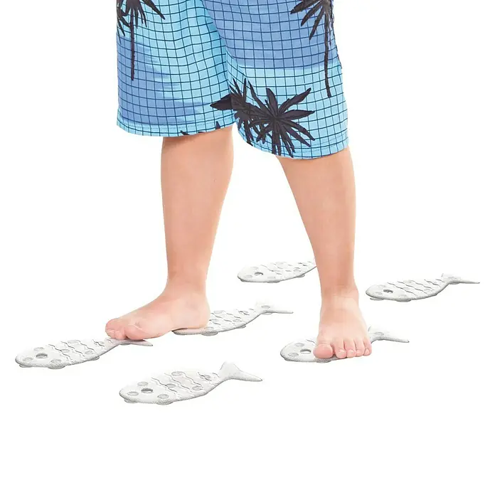 Tatay Antideslizante para bañera Pez - 7 x 15 cm, Transparente - Un niño en bañador está de pie sobre alfombras de baño blancas en forma de pez. Las alfombras tienen un patrón punteado para mayor agarre.