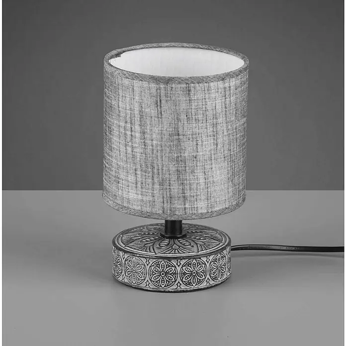 Trio Lighting Lámpara de sobremesa redonda Marie - 28 W, Ø x Al: 13 x 20,5 cm, Gris, E14 - Primer plano de una lámpara de mesa gris con base estampada y pantalla de tela, que emite una luz suave y ambiental.