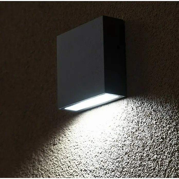 Lutec Aplique exterior LED Gemini XF - 9,5 W, 3,8 x 11 x 11 cm, Gris oscuro, IP54 - Moderna lámpara de pared en forma de cubo hecha de metal oscuro, que proyecta una luz brillante hacia abajo sobre una pared texturizada.