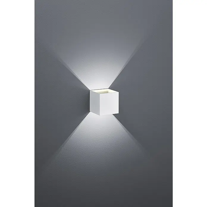 Trio Lighting Aplique de pared Louis - 4,2 W, L x An x Al: 10 x 10 x 10 cm, Blanco - Primer plano de una lámpara de pared cúbica blanca moderna, montada en una pared gris, que emite un brillo suave y dirigido.