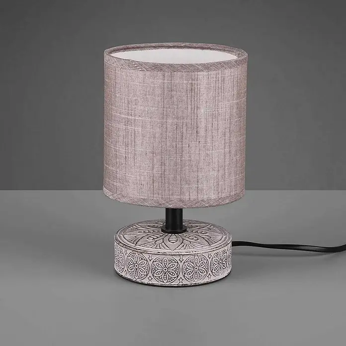 Trio Lighting Lámpara de sobremesa redonda Marie - 28 W, Ø x Al: 13 x 20,5 cm, Marrón, E14 - Una elegante lámpara de mesa con pantalla cilíndrica de tela gris y base redonda blanca con patrones decorativos.