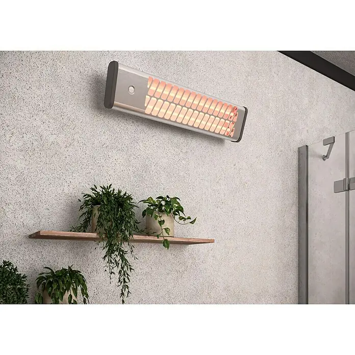 Voltomat HEATING Quarzheizstrahler - 14 x 60 x 13 cm, 1.200 W, Chrom - Nahaufnahme einer an der Wand montierten Heizstrahlers mit warmem Licht, unter dem ein Holzregal mit Grünpflanzen steht.