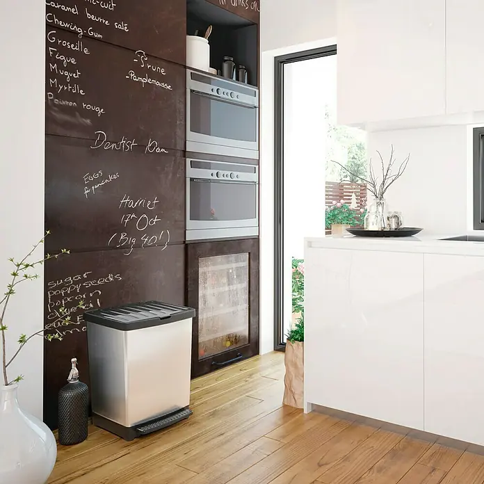 Tatay Cubo con pedal Pedal Trend - 25 l, Plástico, Gris/Negro - Un moderno cubo de basura plateado con tapa negra está en una cocina con pisos de madera y pared de pizarra.