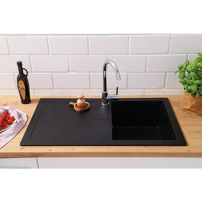 Respekta Einbauspüle Cleveland - 86 x 50 cm, Schwarz - Schwarzes Spülbecken mit Abtropffläche und Armatur auf einer hölzernen Arbeitsplatte, neben einer Flasche Öl und Kräutern.