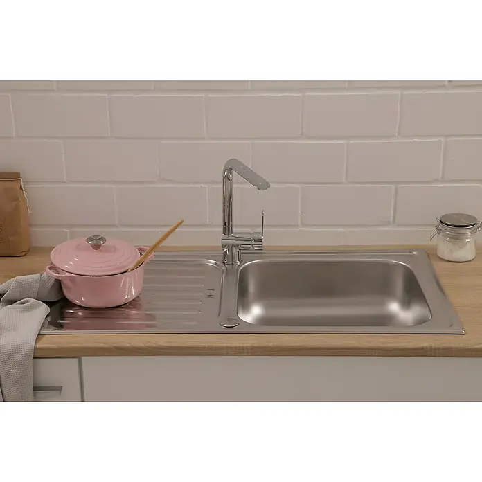 Respekta Einbauspüle Riverside - 100 x 50 cm, Edelstahl - Einbau-Spüle mit Abtropffläche, Hahn, rosa Kochtopf mit Holzlöffel, Glasbehälter mit Zucker und grauem Geschirrtuch auf einer Holzarbeitsplatte.