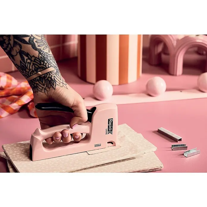 Rapid Handtacker - Feindrahtklammer Typ 53, 4 mm - 10 mm, Rosa - Nahaufnahme eines Rapid Living Tacker in Rosa, der auf Stoff verwendet wird, mit Klammern daneben, inszeniert auf rosa Untergrund.