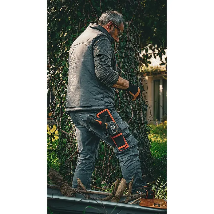 Worx PowerShare 20V Akku-Astsäge WG325E.9 - 20 V, Li-Ionen, Ohne Akku, Schwertlänge: 12 cm - Mann mit Handsäge am Bein in Arbeitskleidung, der im Garten arbeitet.