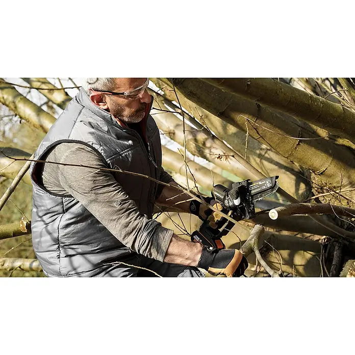 Worx PowerShare 20V Akku-Astsäge WG325E.9 - 20 V, Li-Ionen, Ohne Akku, Schwertlänge: 12 cm - Ein Mann, der eine Akku-Kettensäge benutzt, um Äste zu schneiden. Die Akku-Kettensäge ist kompakt und für den Baumschnitt konzipiert.