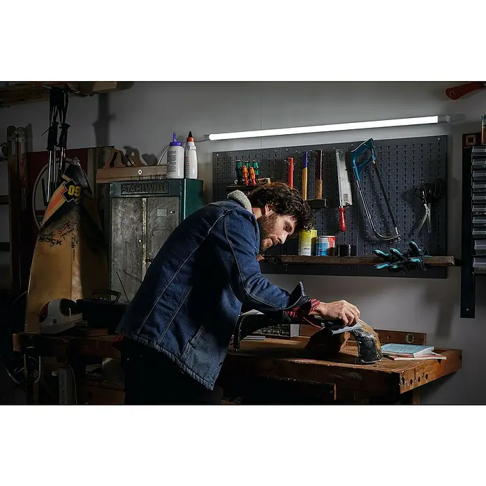 Osram LED Leuchtstoffröhre Tube T8 36 EM UltraLänge: 121,3 cm, Tageslichtweiß, 20 W, 2.400 lm, G13 - Mann schleift ein Werkstück in einer Werkstatt unter einer hellen LED-Leuchte. Die Werkstatt ist mit Werkzeugen ausgestattet.