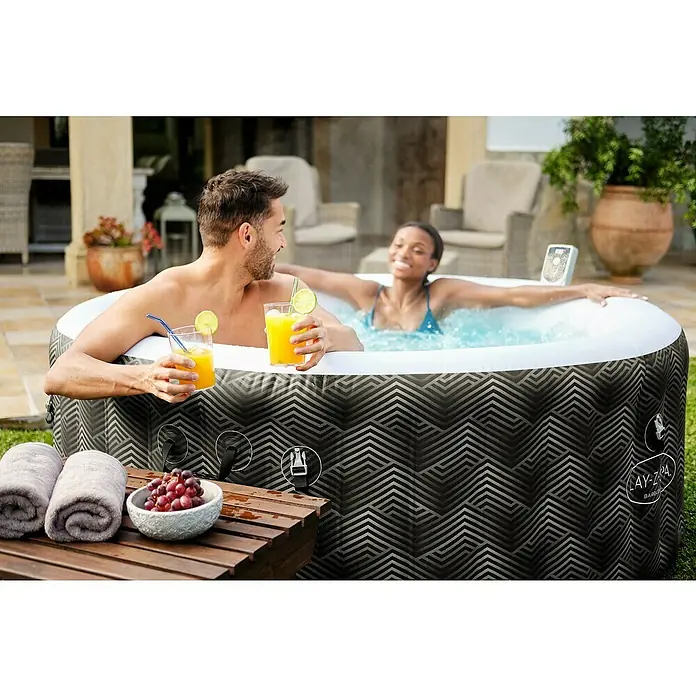Bestway Lay-Z-Spa Mobil-Whirlpool Barbuda AirJet - Ø x H: 180 x 66 cm, Grau, 669 l - Zwei Personen genießen einen Lay-Z-Spa Whirlpool im Freien, mit Getränken und Snacks bereitgestellt. Der Whirlpool ist ein echter Hingucker.