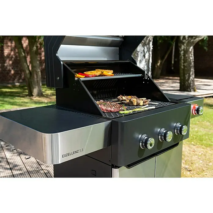 Edelheiss Gasgrill Exzellenz 1.3 - Grillfläche (B x T): 59 x 45,5 cm, 12,6 kW, Anzahl Brenner: 3 Stk. - Nahaufnahme eines EXZELLENZ 1.3 Gasgrills mit Grillgut, der im Freien steht und zum Grillen im Garten einlädt.