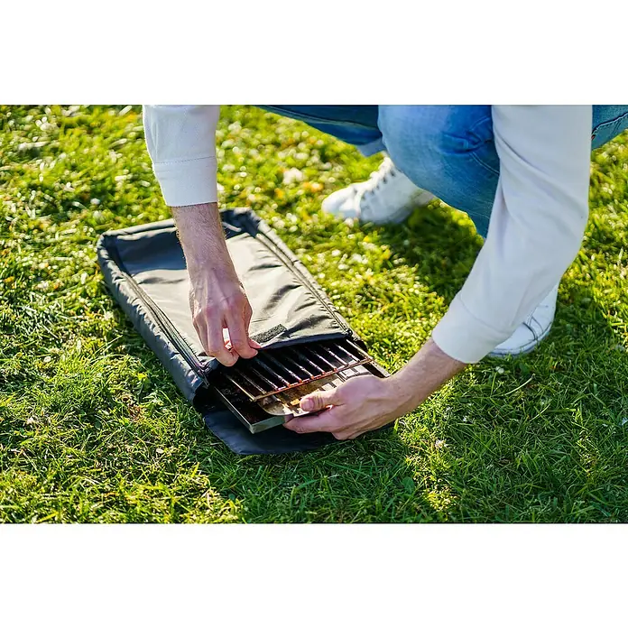 Bruzz Willi Gasgrill BW 1.1 - Wander Edition - Grillfläche (B x T): 39 x 19,5 cm, 3,5 kW, Anzahl Brenner: 1 Stk. - Eine Person packt einen tragbaren Grill aus einer schwarzen Tragetasche auf einer grünen Rasenfläche aus.