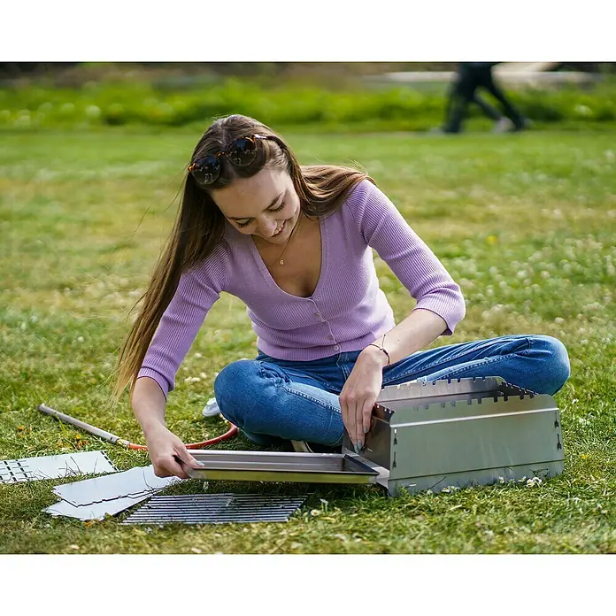 Bruzz Willi Gasgrill BW 1.1 - Wander Edition - Grillfläche (B x T): 39 x 19,5 cm, 3,5 kW, Anzahl Brenner: 1 Stk. - Frau setzt einen neuen Grill im Freien zusammen, um ein tolles Grillfest zu veranstalten.