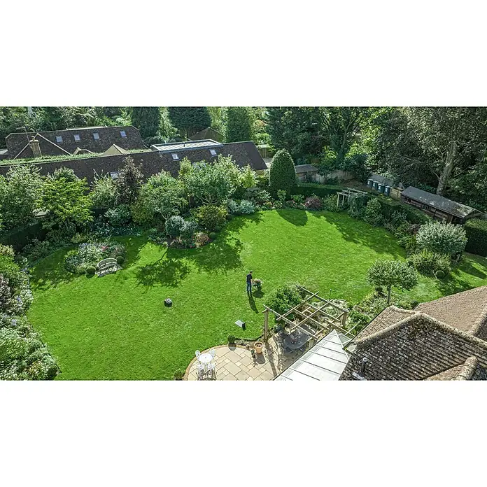Segway Mähroboter Navimow i105E - 500 m², Schnittbreite: 18 cm, Satellitengestützte Navigation, RTK - Luftaufnahme eines weitläufigen Gartens mit gepflegtem Rasen, üppigen Bäumen und einem Gärtner mit Schubkarre.