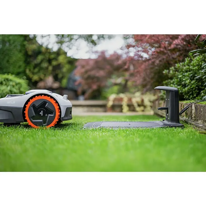 Segway Mähroboter Navimow i105E - 500 m², Schnittbreite: 18 cm, Satellitengestützte Navigation, RTK - Automatisch gesteuerter Rasenmäher vor einer Ladestation im Garten. Der Rasenmäher ist hellgrau und hat orangefarbene Räder.