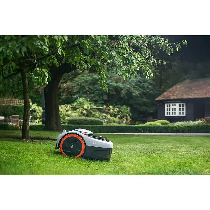 Segway Mähroboter Navimow i105E - 500 m², Schnittbreite: 18 cm, Satellitengestützte Navigation, RTK - Der i105 Rasenmähroboter von Gardena mäht den Rasen. Das Gerät hat orangefarbene Akzente und steht unter einem Baum im Garten.