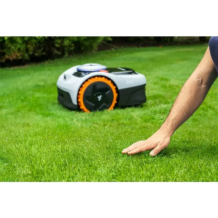 Segway Mähroboter Navimow i105E - 500 m², Schnittbreite: 18 cm, Satellitengestützte Navigation, RTK - Ein Roboter-Rasenmäher auf einem Rasen mit einer Person, die das Gras berührt, um die Rasenqualität zu prüfen.