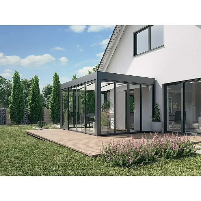 Wismar-NFI Wintergarten - 400 x 300 cm, Satteldach, Polycarbonat, Anthrazitgrau, Milchig Weiß - Helles Bild eines modernen Glasanbaus an ein Haus mit Holzterrasse und blühenden Pflanzen. Der Anbau bietet einen lichtdurchfluteten Wohnraum.