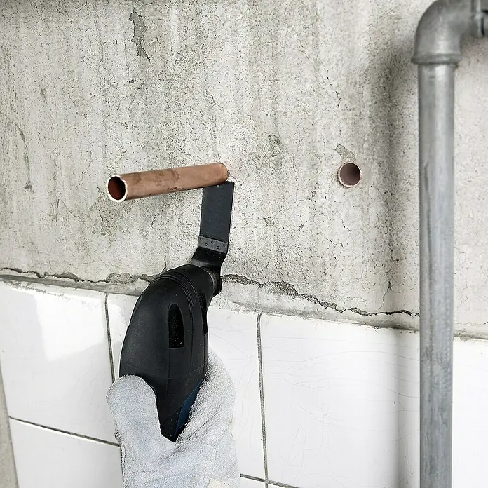 Bosch Zubehör-Set Fliesen - 3 Stk., 3 -tlg. - Ein Oszillierendes Multifunktionswerkzeug schneidet ein Kupferrohr an einer Wand. Ideal für Heimwerkerprojekte und Renovierungsarbeiten.