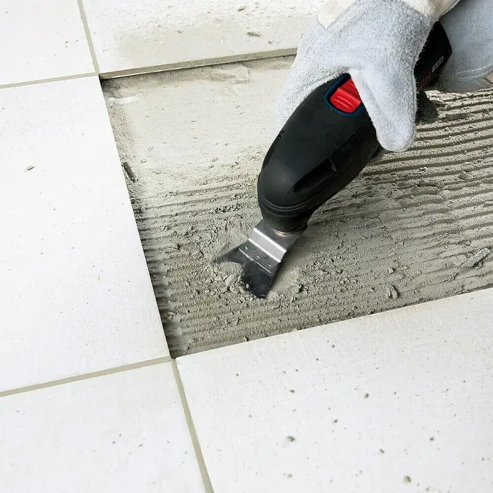 Bosch Zubehör-Set Fliesen - 3 Stk., 3 -tlg. - Entfernung von Fliesenkleber mit einem oszillierenden Werkzeug. Das Werkzeug mit Metallklinge wird von einer Hand mit Schutzhandschuh geführt.