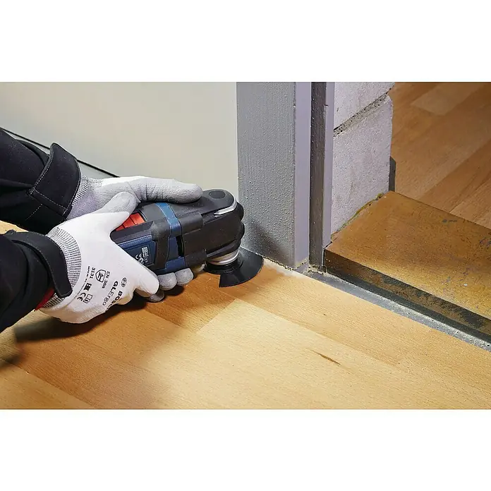 Bosch Installations-Set4 -tlg. - Ein Mann benutzt ein oszillierendes Multifunktionswerkzeug von Bosch mit einem schwarzen Sägeblatt an einem Holzboden neben einer Tür.