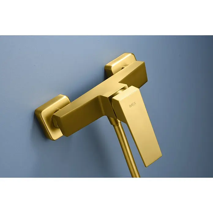 Imex Art Grifo monomando de ducha - Oro - Primer plano de un grifo mezclador de baño IMEX en oro cepillado montado en una pared azul, que muestra un diseño elegante y una artesanía de calidad.