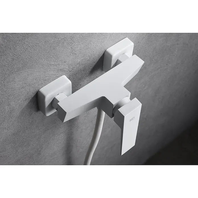 Imex Art Grifo monomando de ducha - Blanco - Primer plano de un grifo de ducha blanco IMEX de líneas limpias montado en una pared gris, que muestra un diseño de baño moderno.