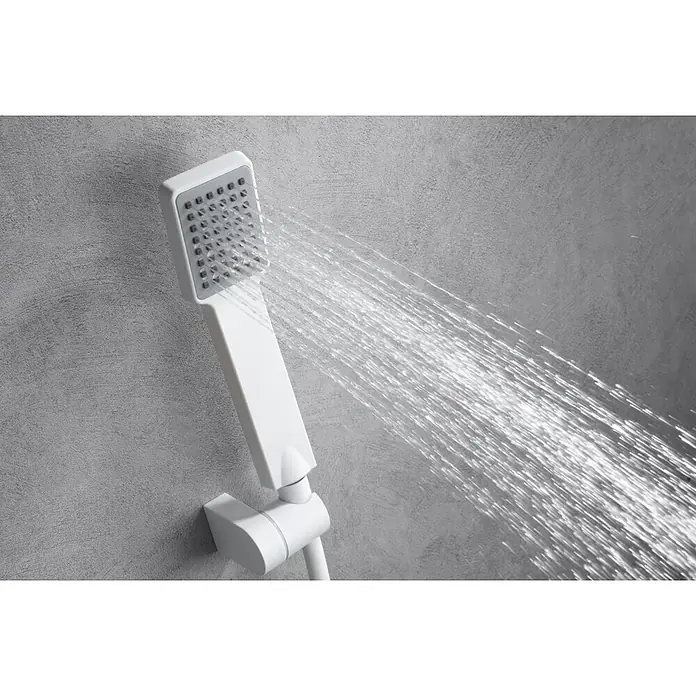 Imex Art Grifo monomando de ducha - Blanco - Un moderno cabezal de ducha de mano blanco con agua pulverizando, sobre una pared gris texturizada. El cabezal es cuadrado.