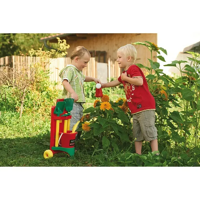 AL-KO Gartenspielgerät Mini Garden Set - Kunststoff, 6 -tlg. - Zwei Kinder gießen Blumen mit einem roten Gießkännchen, während ein Spielzeug-Gartenwagen mit Werkzeugen daneben steht.
