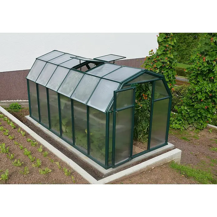 Palram – Canopia Invernadero Eco Grow - Medidas ext. (An x Pr): 204 x 383 cm, 6 mm, Verde - La imagen muestra un invernadero con marcos verdes y paneles transparentes, situado sobre una base de hormigón y rodeado de vegetación.