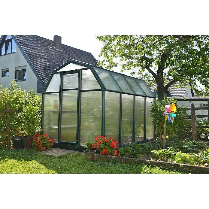Palram – Canopia Invernadero Eco Grow - Medidas ext. (An x Pr): 204 x 239 cm, 6 mm, Verde - Un invernadero de paneles de vidrio con marco verde se encuentra en un jardín junto a la pared de una casa y plantas.