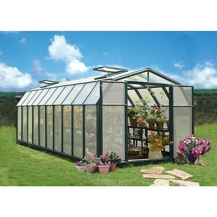Palram – Canopia Invernadero Hobby Gardener - Medidas ext. (An x Pr): 266 x 641 cm, 6 mm, Verde - Un invernadero lleno de plantas, con flores en macetas delante, se alza en un prado verde bajo un cielo azul.