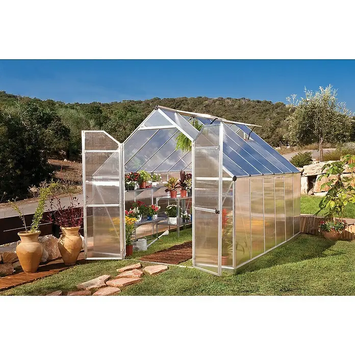 Palram – Canopia Invernadero Essence - Medidas ext. (An x Pr): 244 x 367 cm, Material de la pared lateral: Plástico, 6 mm, Plateado - La imagen muestra un invernadero transparente con puertas abiertas, rodeado de plantas y un jardín bien cuidado.