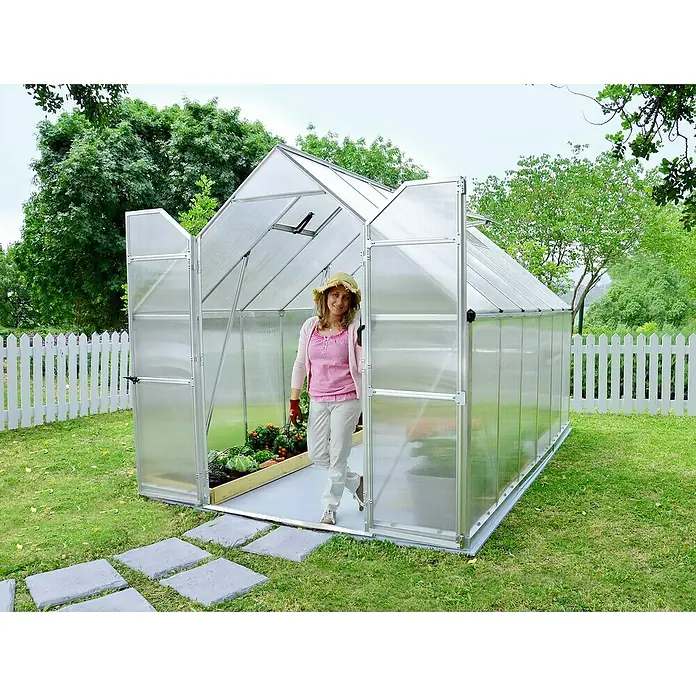 Palram – Canopia Invernadero Essence - Medidas ext. (An x Pr): 244 x 367 cm, Material de la pared lateral: Plástico, 6 mm, Plateado - Mujer entrando en invernadero en el jardín.