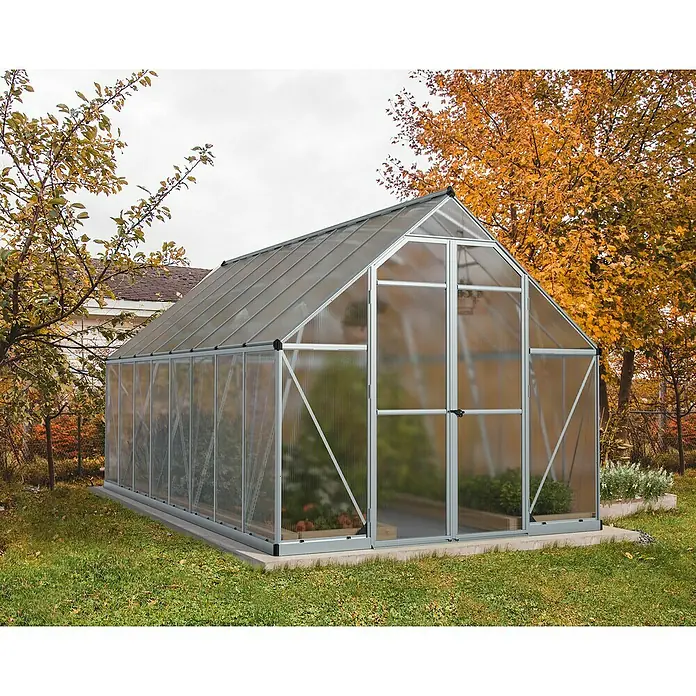 Palram – Canopia Invernadero Essence - Medidas ext. (An x Pr): 244 x 487 cm, Material de la pared lateral: Plástico, 6 mm, Plateado - Un invernadero de metal y paneles transparentes en el jardín, rodeado de árboles.
