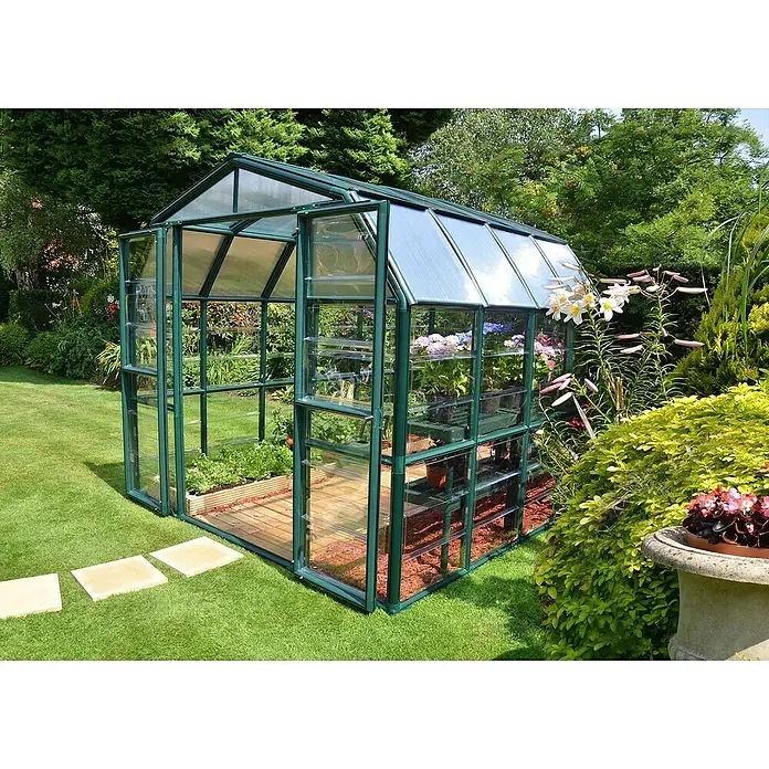 Palram – Canopia Invernadero Grand Gardener - Medidas ext. (An x Pr): 264,7 x 264,2 cm, Material de la pared lateral: Plástico, 0,8 mm, Verde - Un invernadero verde con plantas se alza en un prado verde. El invernadero es de vidrio y metal, con una puerta abierta.