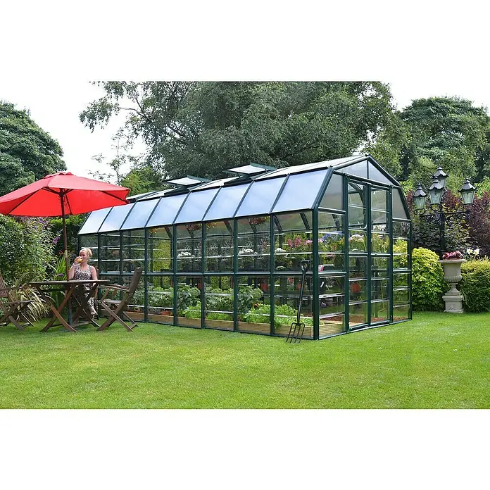 Palram – Canopia Invernadero Grand Gardener - Medidas ext. (An x Pr): 264,7 x 513 cm, Material de la pared lateral: Plástico, 0,8 mm, Verde - Una gran estructura de invernadero de vidrio y metal rodeada de un jardín cuidado con plantas y una sombrilla.