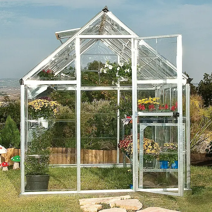 Palram – Canopia Invernadero Harmony - Medidas ext. (An x Pr): 185 x 126 cm, Plateado, Área: 2,3 m² - Un espacioso invernadero de aluminio y cristal con puertas abiertas, lleno de plantas florecientes.