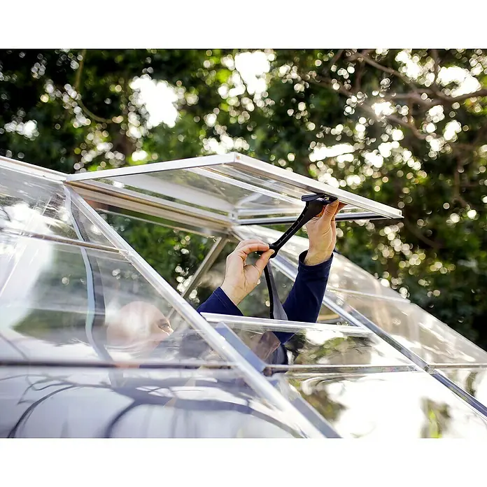 Palram – Canopia Gewächshaus Harmony - Außenmaß inkl. Dachüberstand (B x T): 185 x 426 cm, Silber, Grundfläche: 7,9 m² - Nahaufnahme einer Person, die ein Gewächshausfenster mit einem schwarzen Griff öffnet, wobei der Fokus auf dem Fenster und dem Griff liegt.
