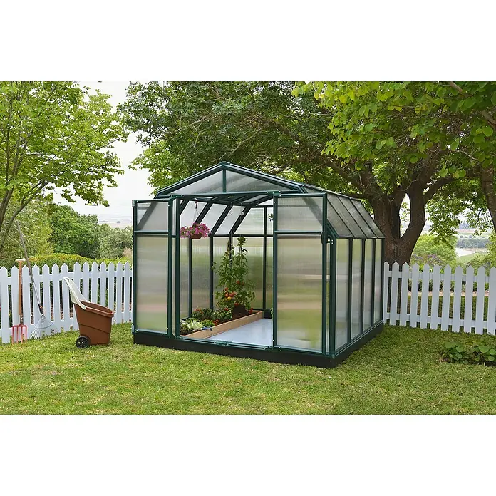 Palram – Canopia Invernadero Hobby Gardener - Medidas ext. (An x Pr): 266 x 266 cm, 6 mm, Verde - Un invernadero con estructura verde se encuentra en el jardín, lleno de plantas de tomate y flores colgantes, con una carretilla cerca.