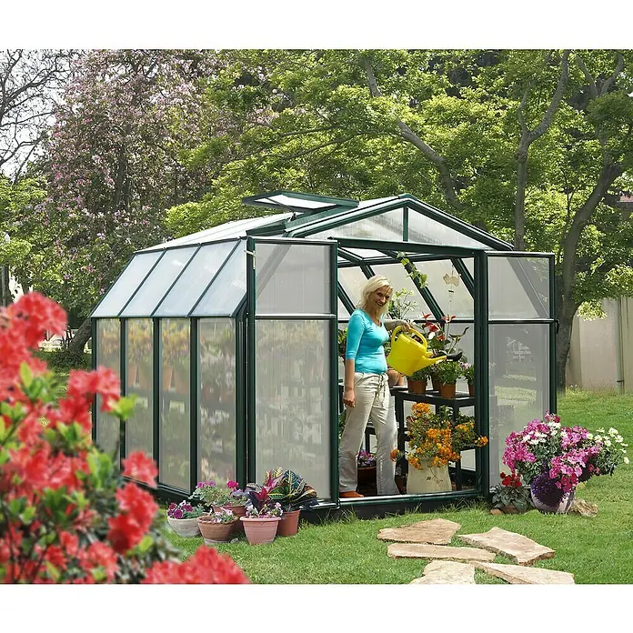 Palram – Canopia Invernadero Hobby Gardener - Medidas ext. (An x Pr): 266 x 266 cm, 6 mm, Verde - Mujer regando plantas en un invernadero rodeado de flores. El invernadero verde tiene paneles transparentes.