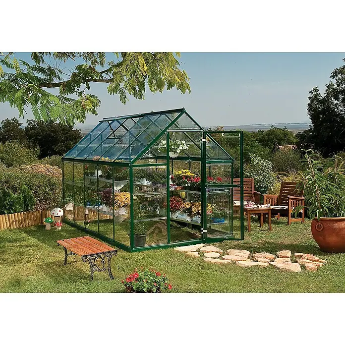 Palram – Canopia Invernadero Harmony - Medidas ext. (An x Pr): 185 x 306 cm, Verde, Área: 5,7 m² - Invernadero en el jardín con puerta abierta, lleno de flores coloridas en estantes. Un banco y muebles de jardín están al aire libre.
