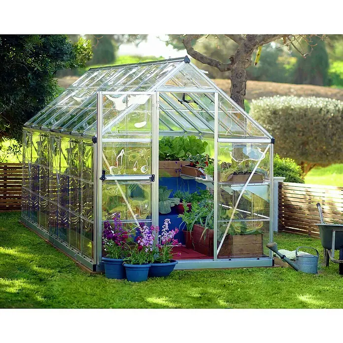 Palram – Canopia Gewächshaus Harmony - Außenmaß inkl. Dachüberstand (B x T): 185 x 426 cm, Silber, Grundfläche: 7,9 m² - Ein Gewächshaus aus Glas und Metall steht im Garten und beherbergt verschiedene Pflanzen in Töpfen und Kisten.