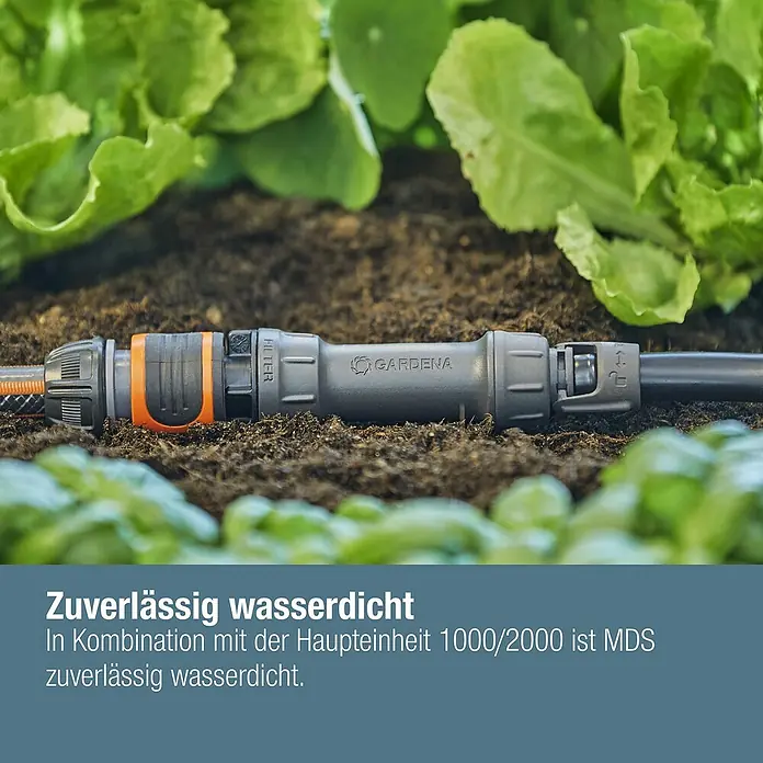 Gardena Micro-Drip Verschlussstopfen 3/16" - 10 Stk., ³⁄₁₆″ - Nahaufnahme eines Gardena-Schlauchverbinders im Gartenbeet, umgeben von grünen Pflanzen.