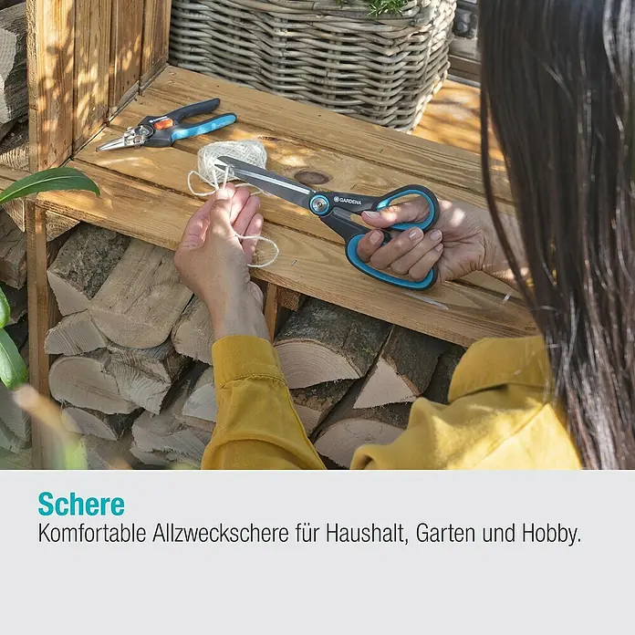 Gardena Universalschere MultiCut - Länge: 22,6 cm - Gardena Universalschere im Einsatz: Schneidet mühelos Garn auf einem Holztisch mit Holzscheiten und einem Weidenkorb im Hintergrund.