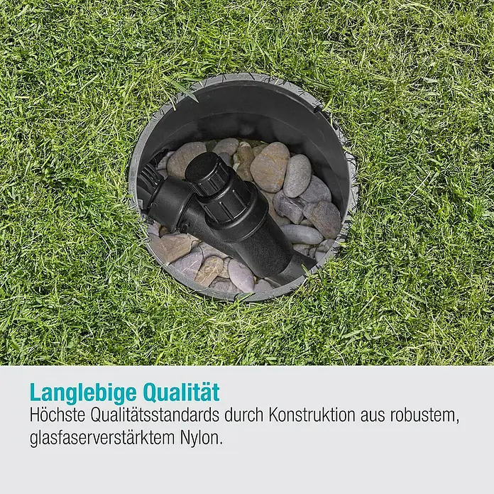 Gardena Sprinklersystem Druckminderer - 1″ - Detailaufnahme eines schwarzen Bewässerungsfilters in einem Erdloch, umgeben von Steinen, eingebettet in grünes Gras.